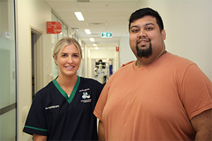 A female physiotherapist stands beside a man in a hospital corridor.