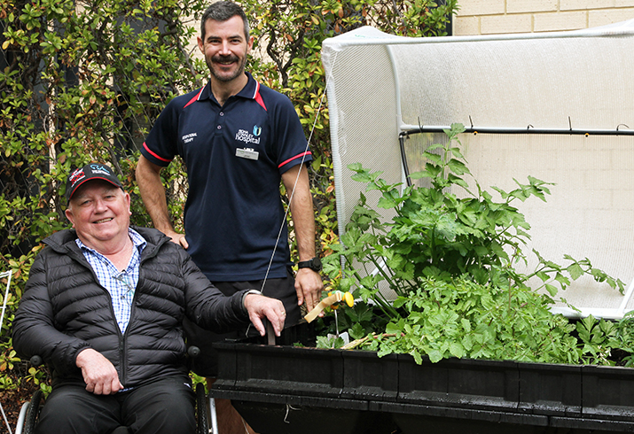 A man in a wheelchair and another man stand beside a raised vegetable garden bed