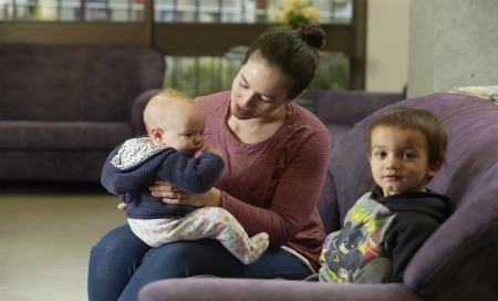 Mother sitting on couch with baby on lap and small child next to her