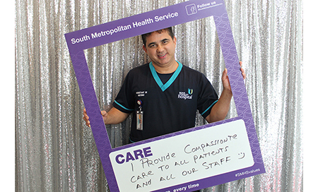  A male nurse holds a sign that reads 'Care – I provide compassionate care to all our patients and all our staff.'