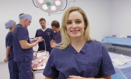 Surgeon in scrubs standing in theatre with team of medical staff in the background