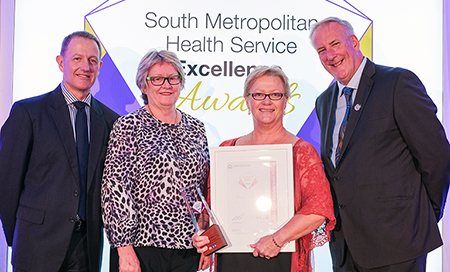 Two men and two women stand in front of a banner that reads South Metropolitan Health Service Awards. One of the women holds a certificate and an award trophy.