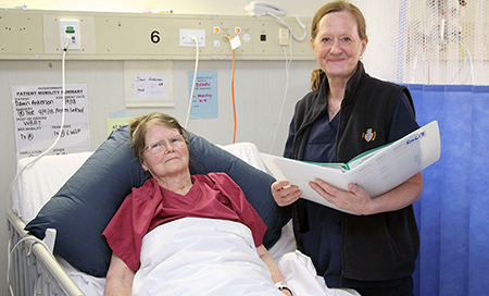 A nurse stands beside a female patient in a hospital bed