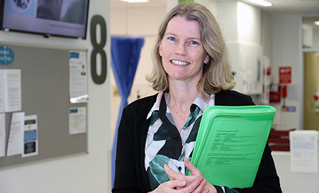 A woman standing in a medical treatment area holding a folder