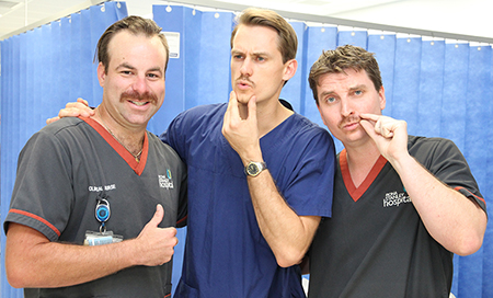 Three men standing together twiddling their moustaches