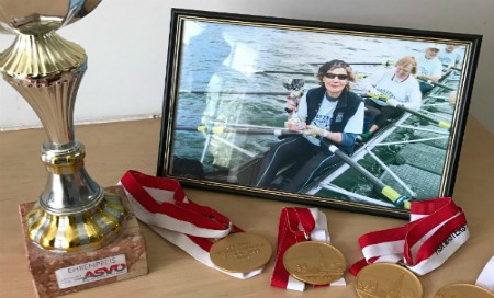 A photo of a woman rowing with four medals and a trophy in front of it
