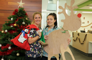 Two female Radiation Oncology staff holding a Santa sack and a cardboard reindeer