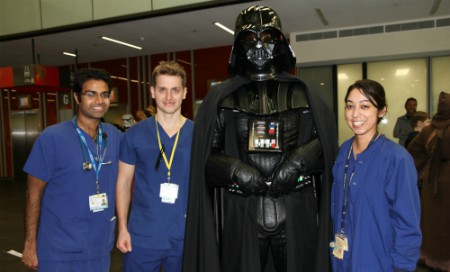 Three staff members wearing scrubs alongside person in Darth Vader costume