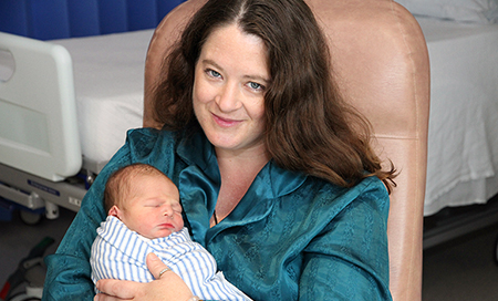 A woman seated in a chair holds a newborn baby.