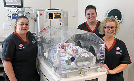 Three female clinical nurses stand beside a newborn baby in an incubator