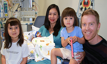 A woman holds a small newborn baby while two young children and a man sit beside her.