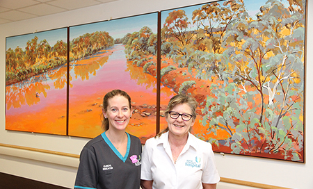 Two female nurses stand in front of a large, colourful artwork